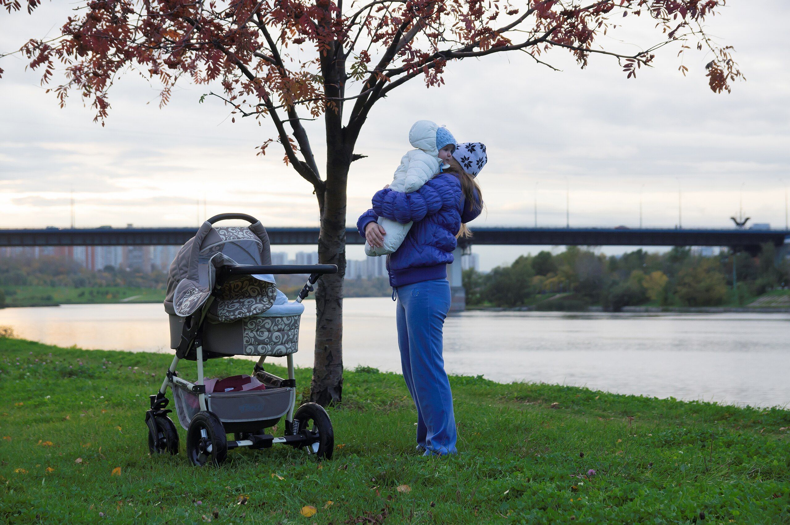 person holding child while stood next to tree and river